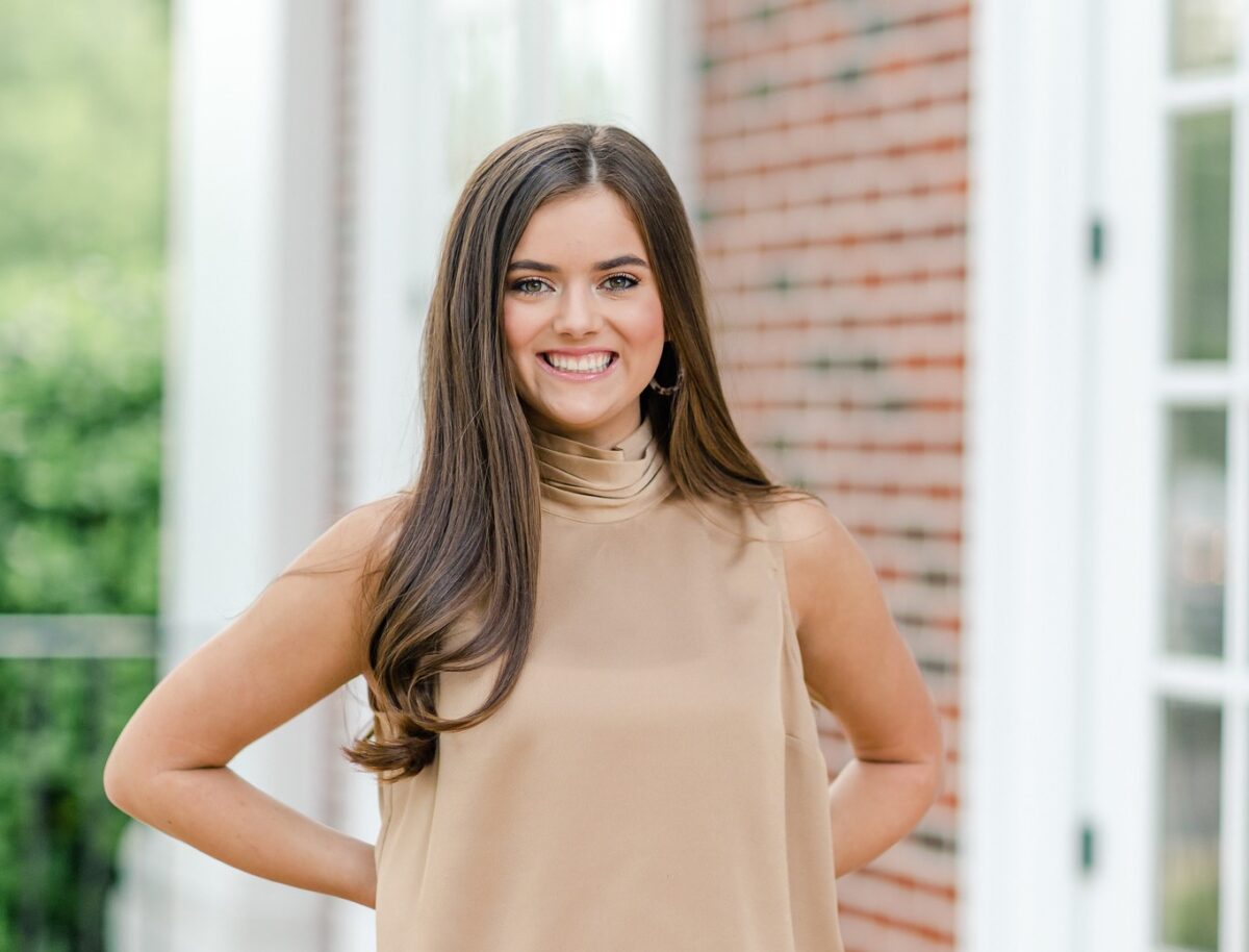 Student in real estate office, holding tablet with property listings, smiling.