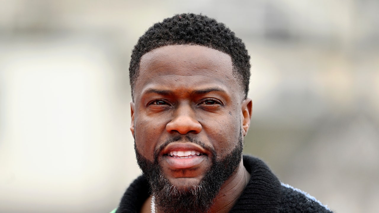 Kevin Hart standing in front of luxury mansion with city skyline behind him.