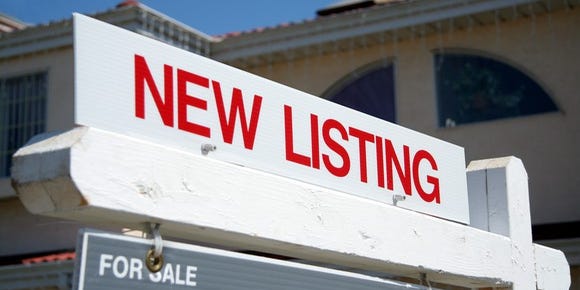 Homeowner standing in front of house with 'For Sale by Owner' sign.