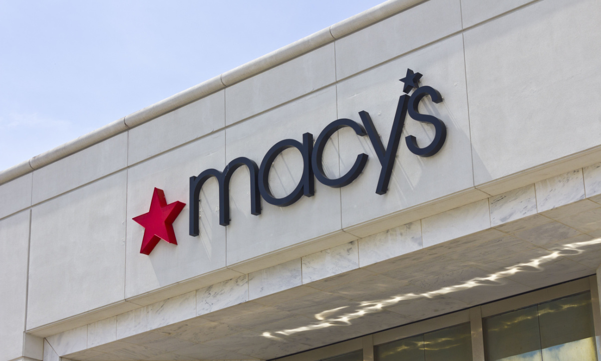 Macy's logo on store front with rising stock market graph.