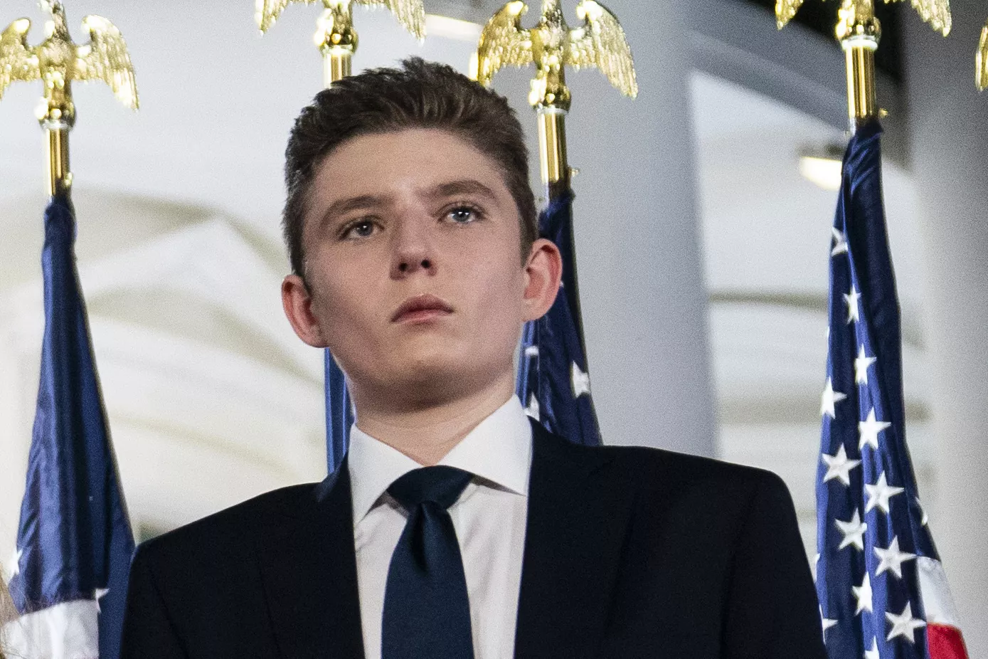 Barron Trump stands in front of luxury real estate development, smiling.