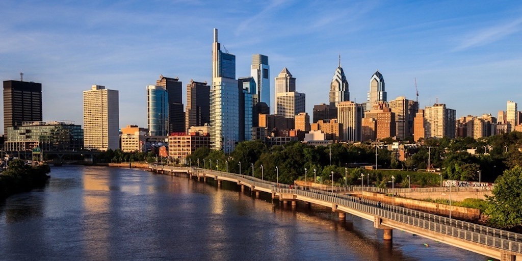 Philadelphia cityscape with real estate market charts and graphs on screen.